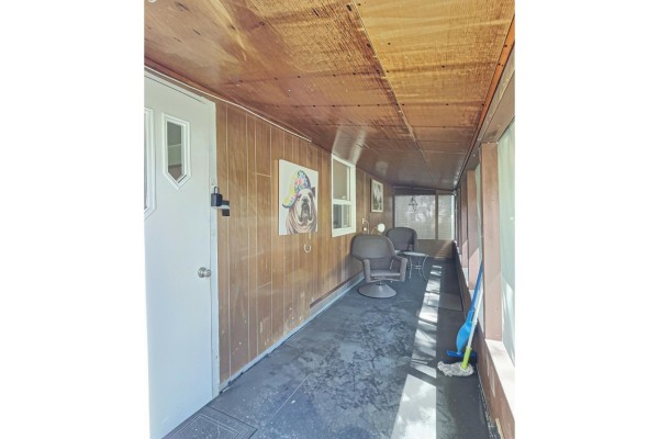 Covered porch with wood-paneled walls, dark flooring, two chairs, and a door leading inside. - 342c Ch. De Sand Bay, Clarendon