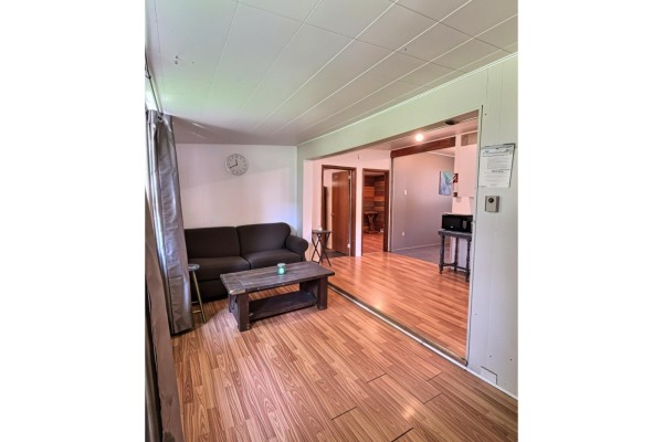 Living room with a dark sofa, wooden coffee table, and hardwood floors, opening to another room. - 342c Ch. De Sand Bay, Clarendon