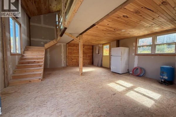 Interior of unfinished cabin with wooden stairs, exposed beams, plywood floors, and a white refrigerator. - 343 Hilltop Road, Hilltop
