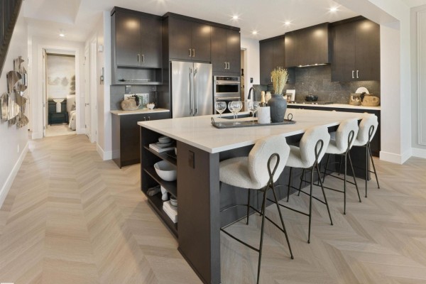 Modern kitchen with dark cabinetry, stainless steel appliances, island with white countertop, and bar stools. - 344 Stiles Wy, Leduc