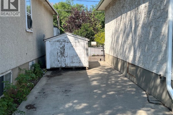 Side yard with a concrete path between the bungalow and a neighboring house, featuring a shed. - 344 Wascana Street, Regina