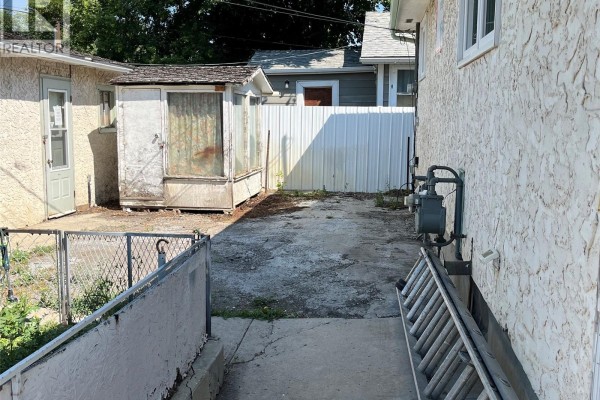 Backyard view with a concrete pad, a small greenhouse-like shed, and a gas meter on the house exterior. - 344 Wascana Street, Regina