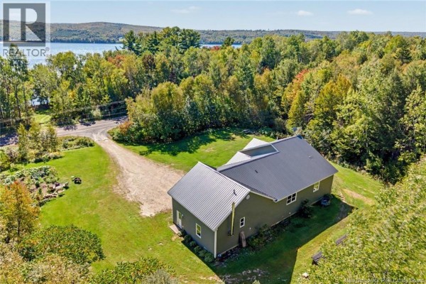 Aerial view of a green house with a dark metal roof, surrounded by grass and trees, with a lake in the distance. - 3442 Route 105, Bear Island