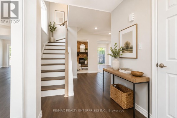 Entrance hall with a staircase, dark hardwood floors, beige walls, and framed art on the wall. - 3446 Ash Row Crescent N, Mississauga