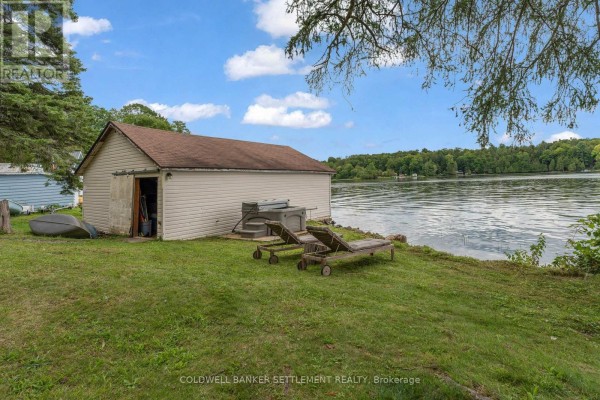 View of a detached garage and waterfront with two lounge chairs on the grass. - 345 Battams Road, Rideau Lakes