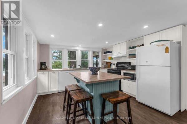 Kitchen with white cabinetry, a light blue island with wooden stools, and windows. - 345 Battams Road, Rideau Lakes