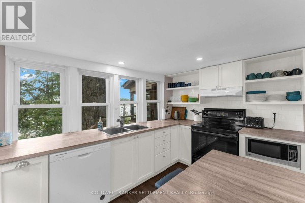 Kitchen featuring white cabinets, a double sink, dishwasher, stove, and microwave. - 345 Battams Road, Rideau Lakes