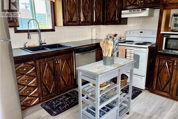 Kitchen with dark wood cabinets, white countertops, white appliances, and a portable island. - 345 Renfrew, Dalhousie