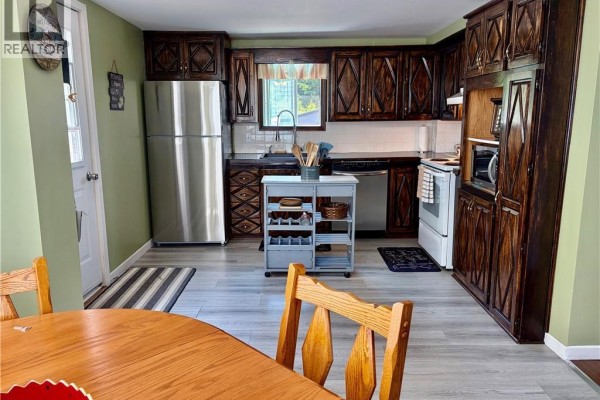 Kitchen with a stainless steel refrigerator, dark wood cabinets, and a wooden dining table. - 345 Renfrew, Dalhousie