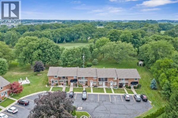 Aerial view of a brick townhouse complex with parking lot and surrounding mature trees. - 345 Robson Road Unit# 18, Leamington