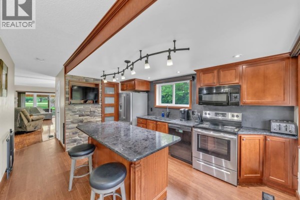 Kitchen with granite island, wooden cabinets, stainless steel appliances, and stone accent wall with TV. - 345 Robson Road Unit# 18, Leamington
