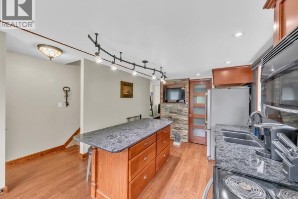 Kitchen with granite island, wooden cabinets, stainless steel appliances, and view of living room staircase. - 345 Robson Road Unit# 18, Leamington