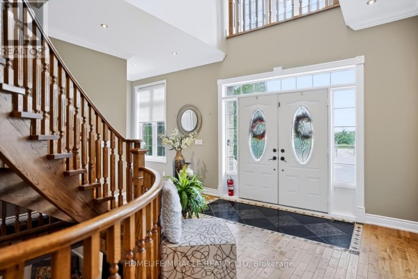 Spacious entryway with a grand wooden staircase, double white doors with glass inserts, and hardwood floors. - 345305 15th Side Road, Mono