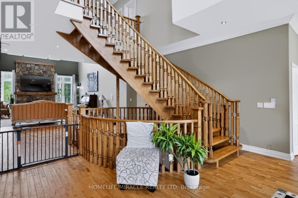 View of the open-concept living area with a stone fireplace and a large wooden staircase. - 345305 15th Side Road, Mono