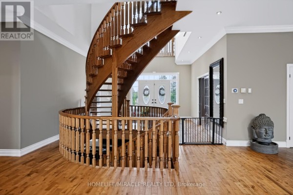 Interior view of the foyer featuring a curved wooden staircase, double doors, and hardwood flooring. - 345305 15th Side Road, Mono
