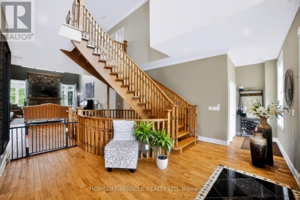 Sunlit foyer with a central wooden staircase, hardwood floors, and a view into the living area. - 345305 15th Side Road, Mono