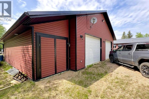 Side view of the garage with a vehicle parked in front and landscaped area. - 346, 14579 Twp Rd 690, Lac La Biche