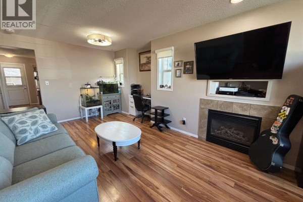 Living room with a sofa, coffee table, fireplace, mounted television, and a desk with a computer. - 346 Boutin Avenue, Hinton