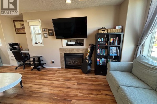 Living room showing the sofa, fireplace, television, bookshelves, and a desk area with a computer. - 346 Boutin Avenue, Hinton