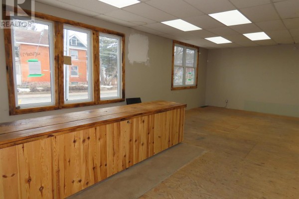 Interior room with a long wooden counter, large windows, and beige walls. - 346 North St, Sault Ste Marie