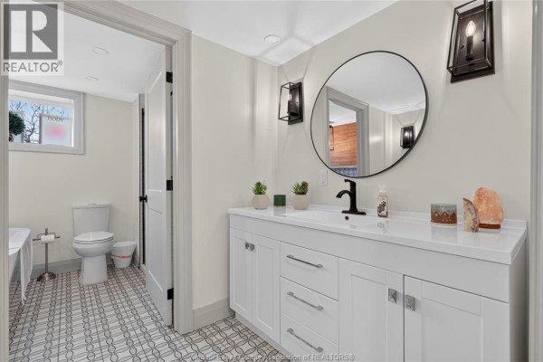 Modern bathroom with white vanity, round mirror, and decorative floor tiles - 346 Texas Road Amherstburg