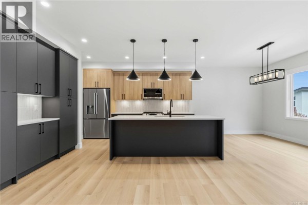 Bright kitchen and dining area with light wood floors, dark grey and wood cabinets, and stainless steel appliances. - 3462 Merlot Terr, Langford