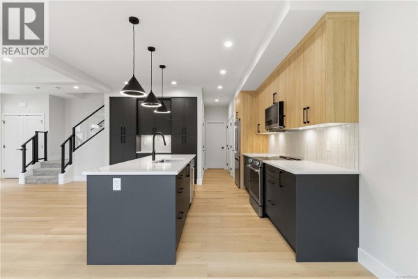 Kitchen with a large dark grey island, white countertops, wood upper cabinets, and a staircase to the side. - 3462 Merlot Terr, Langford