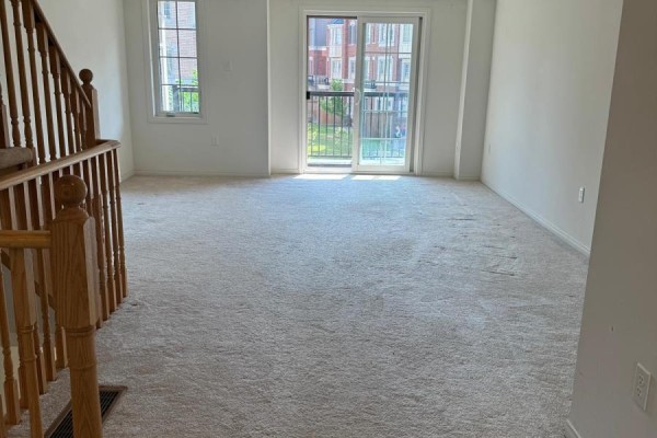View of a carpeted living room with a sliding glass door and wooden staircase. - 347 - 2370 Chevron Prince Path W, Oshawa