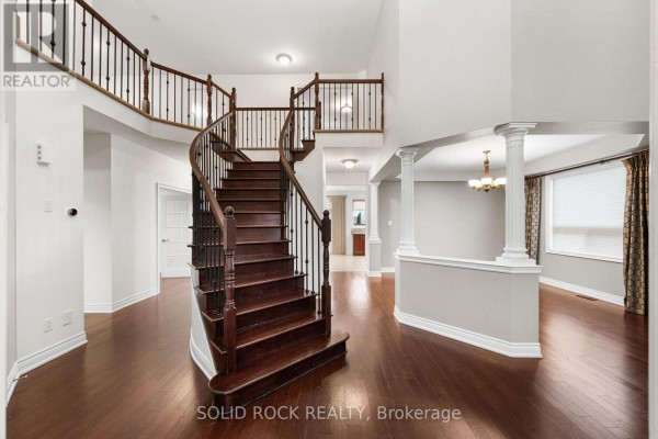 Grand staircase with dark wood treads and a black metal balustrade in a foyer with hardwood floors. - 347 Bamburgh Way, Ottawa