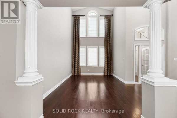 Living room with floor-to-ceiling windows, dark hardwood floors, and decorative columns framing the entrance. - 347 Bamburgh Way, Ottawa