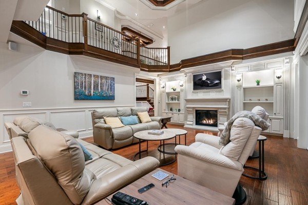 Living room with cream leather sofas, fireplace, entertainment center, wood floors, and a view of the upper balcony. - 3472 164a Street, Surrey