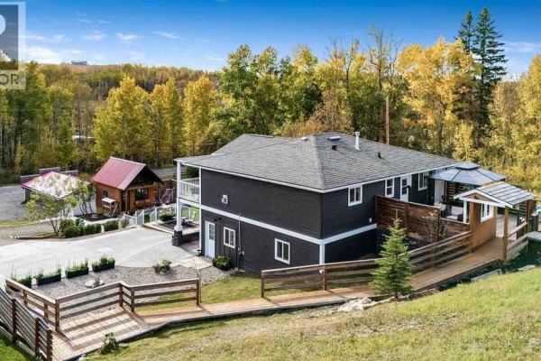 Rear view of dark gray house with decks, gazebo, and surrounding trees. - 3472c Township Road 290 A, Rural Mountain View County