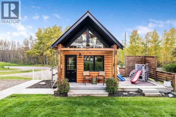 Small log cabin with a red metal roof and a children's playset. - 3472c Township Road 290 A, Rural Mountain View County
