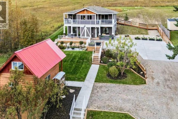Aerial view of a dark gray house, red-roofed cabin, and landscaped yard. - 3472c Township Road 290 A, Rural Mountain View County