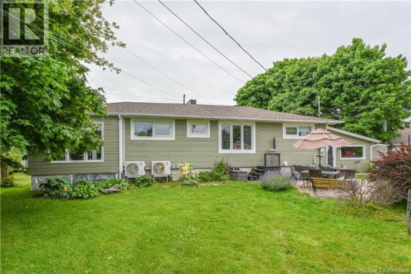 Rear exterior view of the light green house with a green lawn and patio. - 3480 Centenaire Street, Tracadie