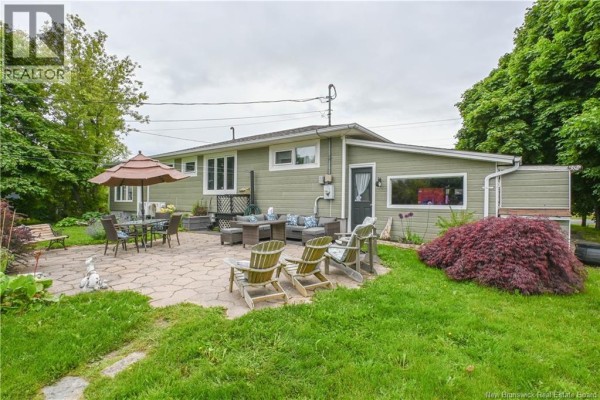 Rear patio area with outdoor furniture, umbrella, and surrounding greenery. - 3480 Centenaire Street, Tracadie