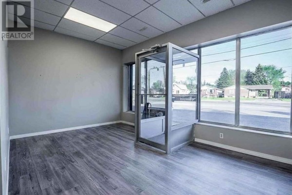 Interior view of an empty commercial space with grey walls, wood-look flooring, and large front windows. - 3481 Falconbridge Highway Unit# 3, Sudbury