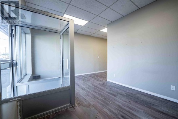 Interior view of an empty commercial space with grey walls, wood-look flooring, and a glass reception area. - 3481 Falconbridge Highway Unit# 3, Sudbury