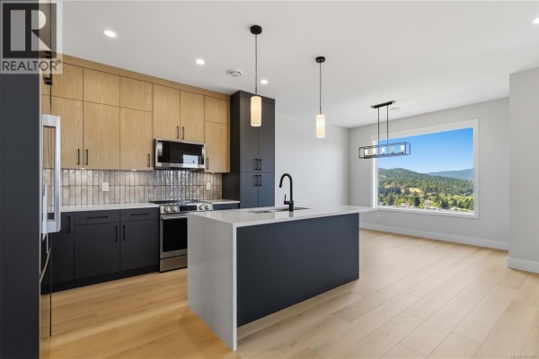 Modern kitchen with dark grey lower cabinets, light wood uppers, and a large island with a white countertop. - 3482 Merlot Terr, Langford