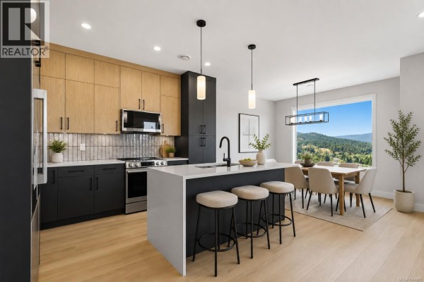 Open concept kitchen and dining area with a large window view of rolling hills and trees. - 3482 Merlot Terr, Langford