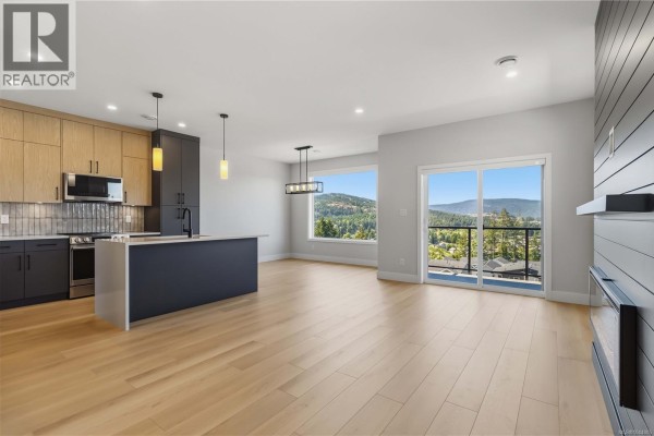 Open concept living area with kitchen, dining, and sliding glass doors to a balcony overlooking a valley. - 3482 Merlot Terr, Langford