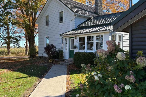 Two-story farmhouse with white siding, green roof, and large trees in the yard. - 349 20 Side Road, Kincardine