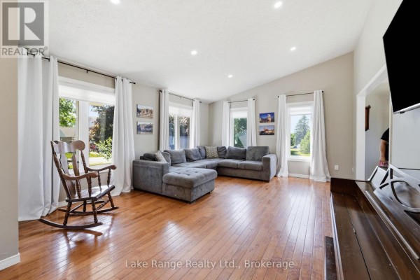 Living room with a large grey sectional sofa, hardwood floors, and a rocking chair. - 349 South Delhi Street, Huron Kinloss