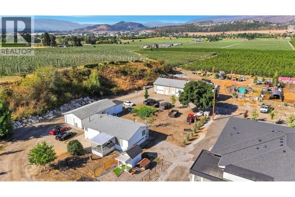 Aerial view of a property with multiple outbuildings, parked vehicles, and agricultural fields. - 3490 Old Vernon Road, Kelowna