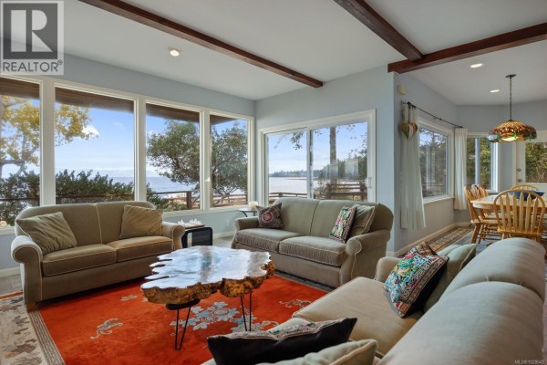 Bright living room with large windows, two sofas, and a unique coffee table. - 3495 Harwood Rd, Hornby Island