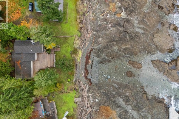 Aerial view of the property showing the house, deck, and rocky coastline. - 3495 Harwood Rd, Hornby Island