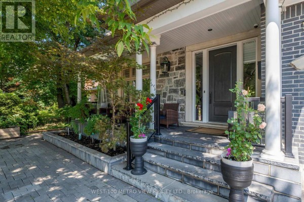 Covered front porch with stone columns, a dark front door, and potted plants. - 3495 Joan Drive, Mississauga