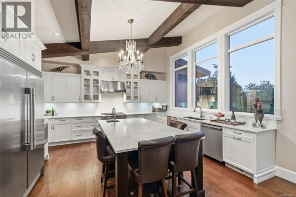 Spacious white kitchen with island, wood beams, and stainless steel appliances. - 3495 Simmons Pl, Nanoose Bay