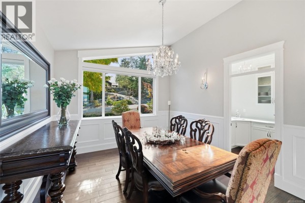 Formal dining room with dark wood table, ornate chandelier, and wainscoting. - 3495 Simmons Pl, Nanoose Bay