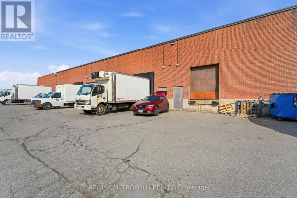 Loading dock area with trucks, a car, and pallets outside a brick building. - 35 - 120 Dynamic Drive, Toronto